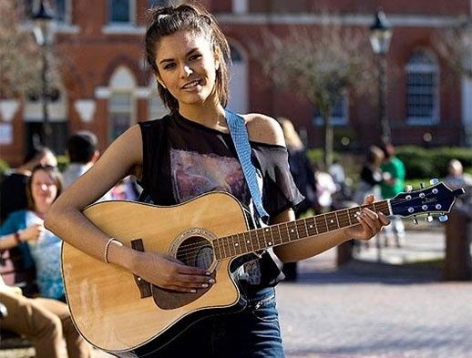 Gademusiker spiller akustisk guitar foran en travl byplads