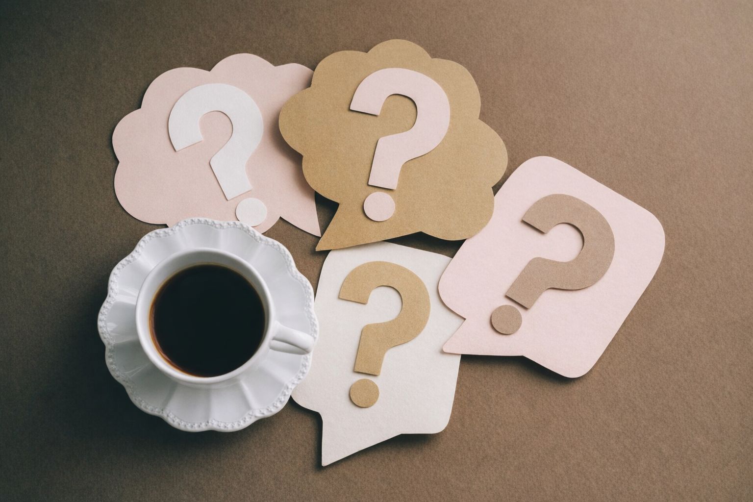 Spørgsmålstegn på talebobler ved siden af en kop kaffe.